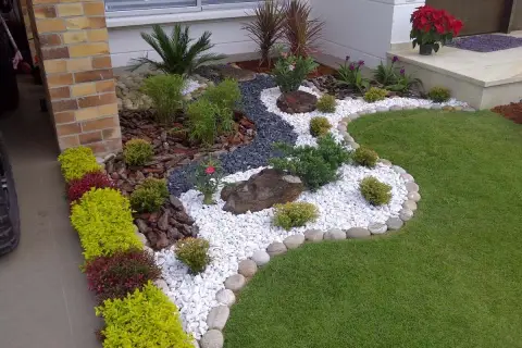 Un giardino moderno e curato, con ghiaia bianca, pietre, piante verdi e fiori rossi. Un esempio di come rifare un giardino con stile.